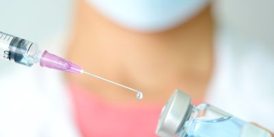 doctor's hand holds a syringe and a blue vaccine bottle at the hospital. Health and medical concepts