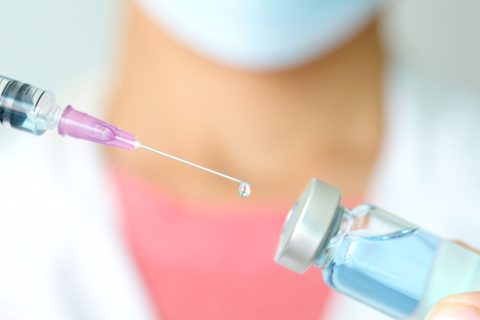doctor's hand holds a syringe and a blue vaccine bottle at the hospital. Health and medical concepts