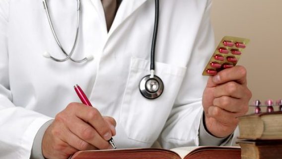 Doctor holding up pills and writing in a book