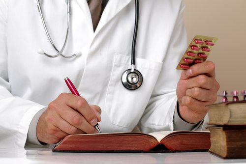 Doctor holding up pills and writing in a book