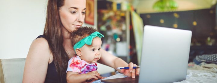 Woman holds her baby while at the computer