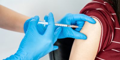 Syringe injection being placed into an arm. Provider wears blue gloves.