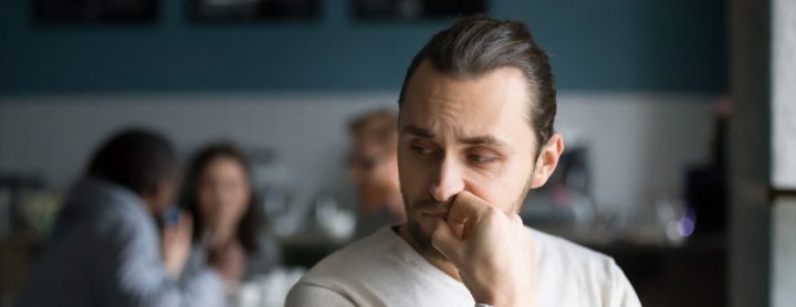 Man sitting nervously in coffee shop with other people