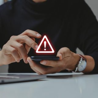 A person holding a smartphone displaying a glowing red warning triangle symbol