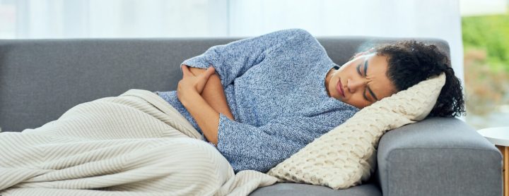 Woman holding her stomach in pain while lying on the couch