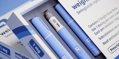 Box of semaglutide weight loss injection pens with five blue single-dose pens, one shown with needle exposed.