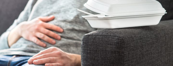 Man with stomach pain on couch sitting next to takeout box