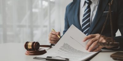 Attorney in a navy suit reviewing legal documents beside a wooden gavel and brass scales of justice.