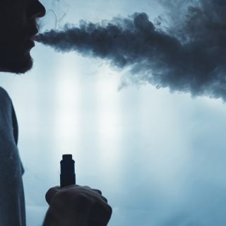 A bearded man vaping with a cloud of smoke