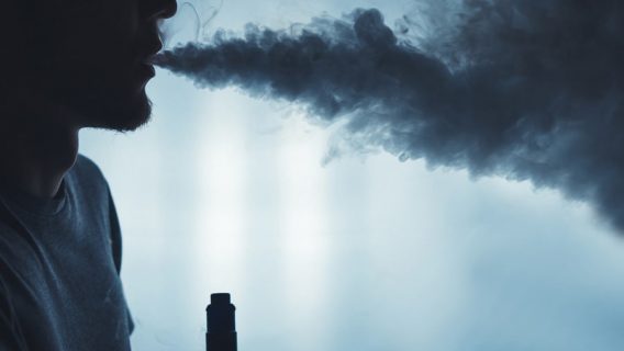 A bearded man vaping with a cloud of smoke