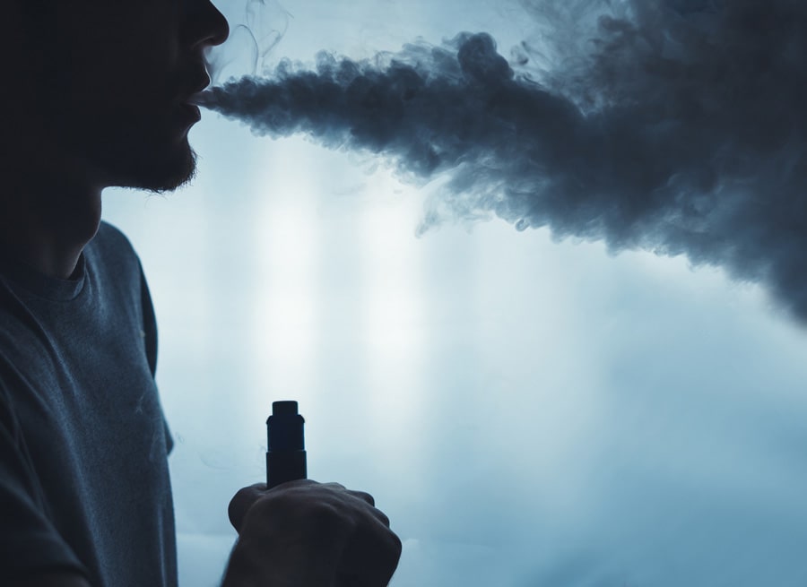 A bearded man vaping with a cloud of smoke
