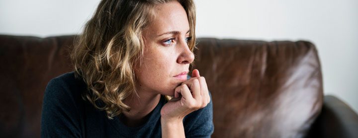 Sad woman sits on her couch and stares