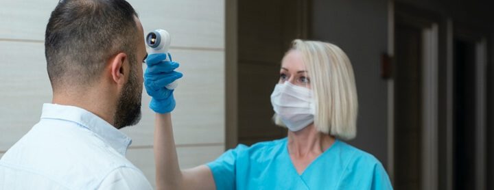 Doctor checking patient's temperature with infrared tool at a hospital