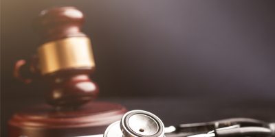 Stethoscope with a blurred wooden gavel with gold trim in the background.