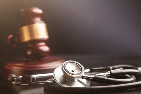 Stethoscope with a blurred wooden gavel with gold trim in the background.