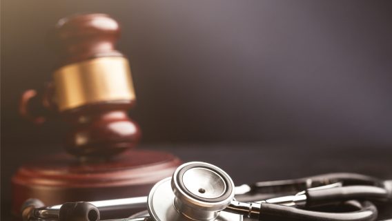 Stethoscope with a blurred wooden gavel with gold trim in the background.