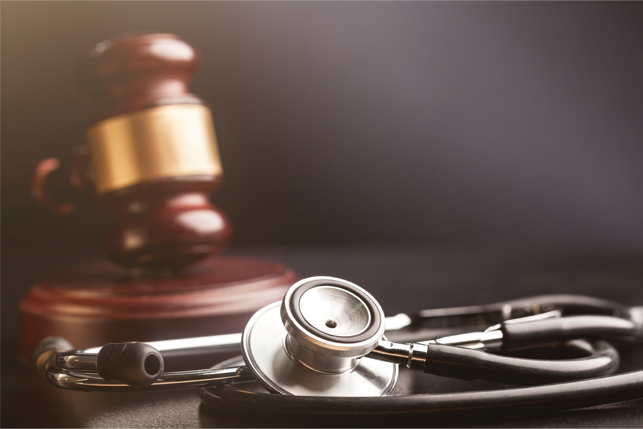 Stethoscope with a blurred wooden gavel with gold trim in the background.