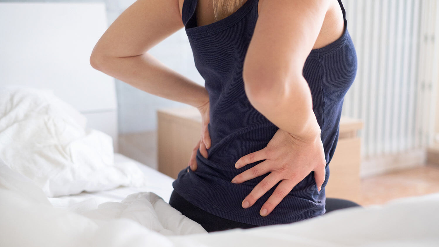 Woman holding her hips while sitting on a bed.