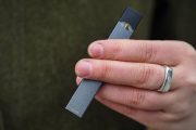 hand with silver ring holding a Juul vaping device
