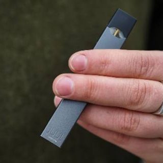 hand with silver ring holding a Juul vaping device