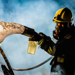 Firefighter extinguishing car fire with foam spray