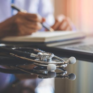 Doctor writing with a stethoscope on desk