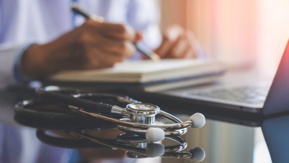 Doctor writing with a stethoscope on desk