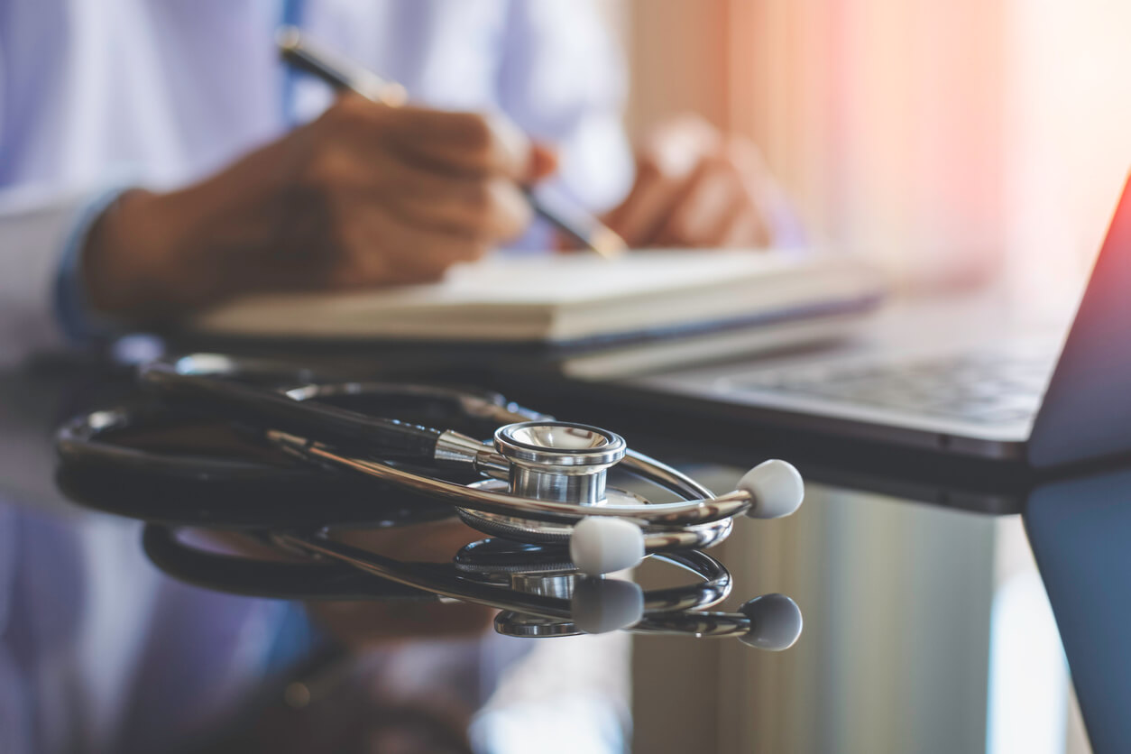 Doctor writing with a stethoscope on desk