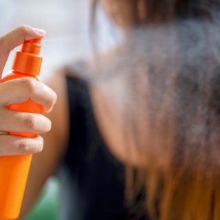 Young woman applying hair spray in bathroom