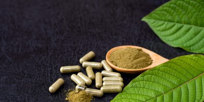 kratom capsules next to plant leaves
