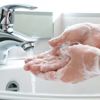 Hands being washed with soap in a running sink.