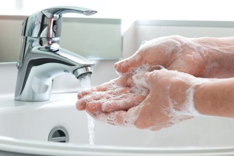 Hands being washed with soap in a running sink.