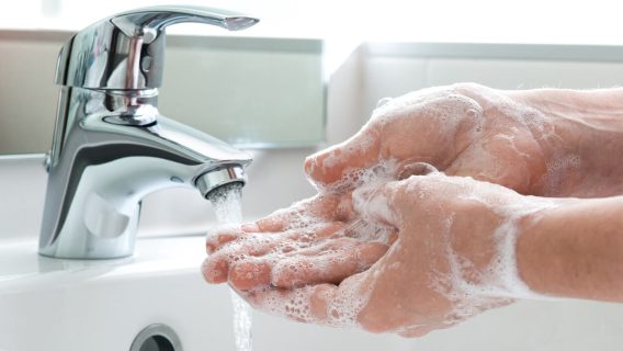 Hands being washed with soap in a running sink.