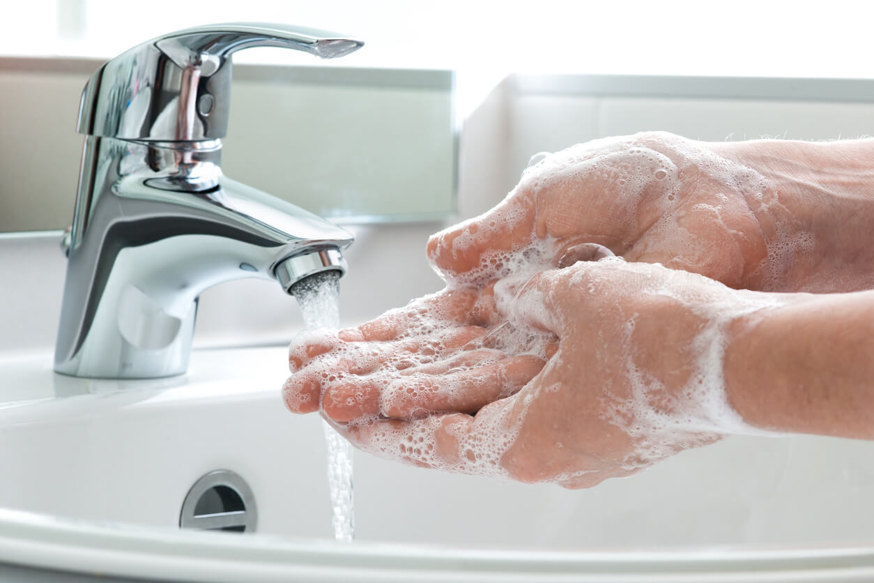 Hands being washed with soap in a running sink.
