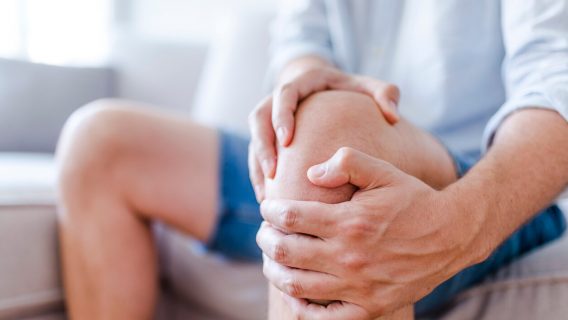 Man suffering from knee pain sitting on sofa