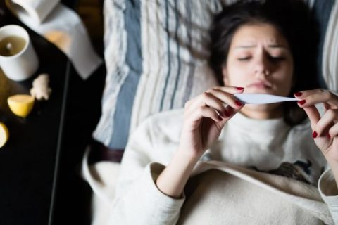 Woman laying in bed holding thermometer