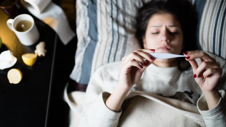 Woman laying in bed holding thermometer