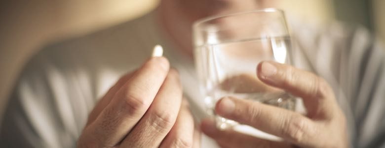 person holding a pill and a cup of water