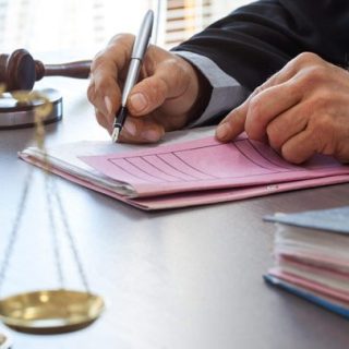 judge signing a doc with scales of justice and gavel on the table