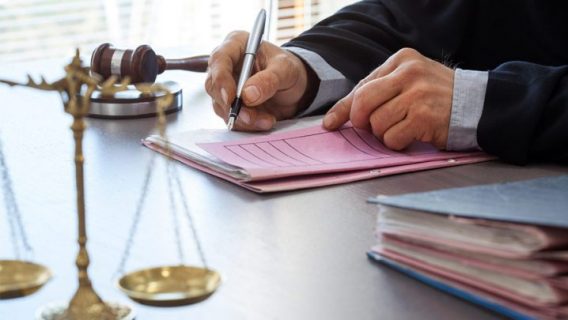 judge signing a doc with scales of justice and gavel on the table