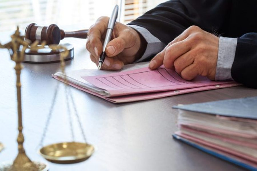 judge signing a doc with scales of justice and gavel on the table