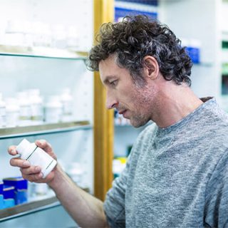 man reading a pill bottle in a pharmacy