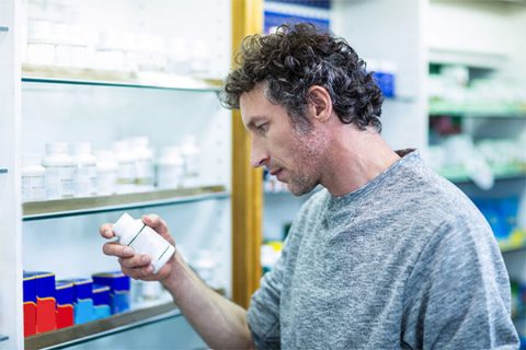 man reading a pill bottle in a pharmacy