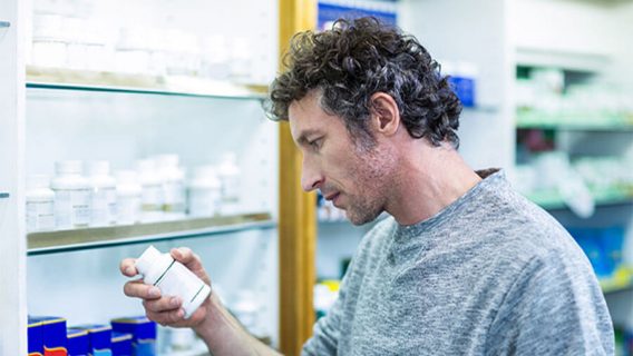 man reading a pill bottle in a pharmacy