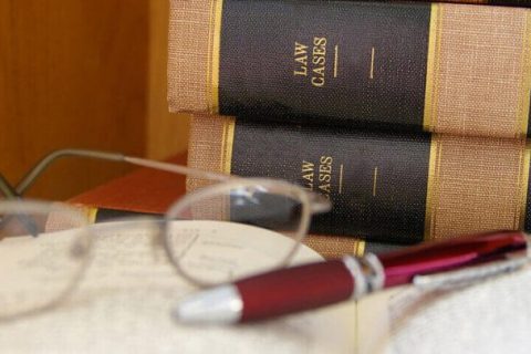 law books with one opened with glasses and a pen resting on top