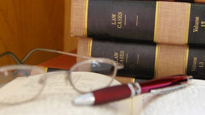 law books with one opened with glasses and a pen resting on top