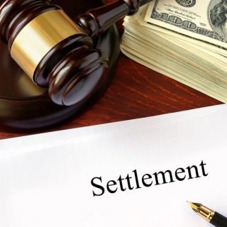 gavel with a stack of hundred dollar bills over a settlement form