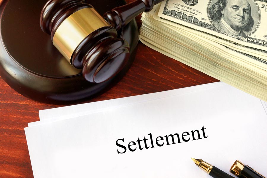gavel with a stack of hundred dollar bills over a settlement form