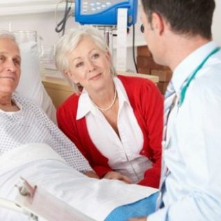 doctor visiting elderly man in his hospital room and his wife