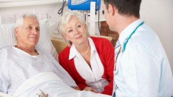 doctor visiting elderly man in his hospital room and his wife
